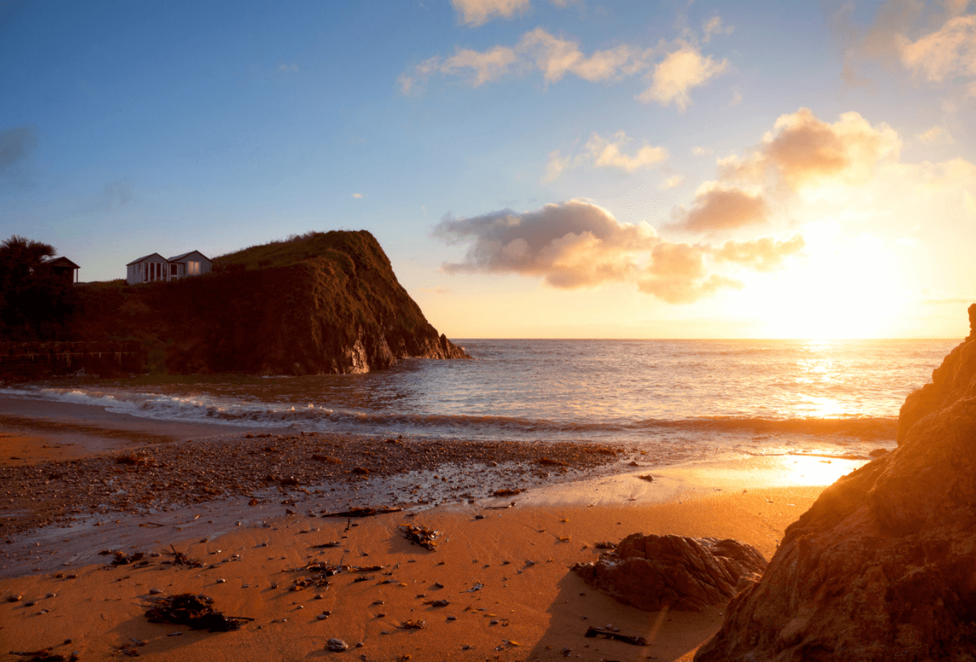 Beach huts on the cliff tops with the sun setting over Hope Cove, Devon, England.